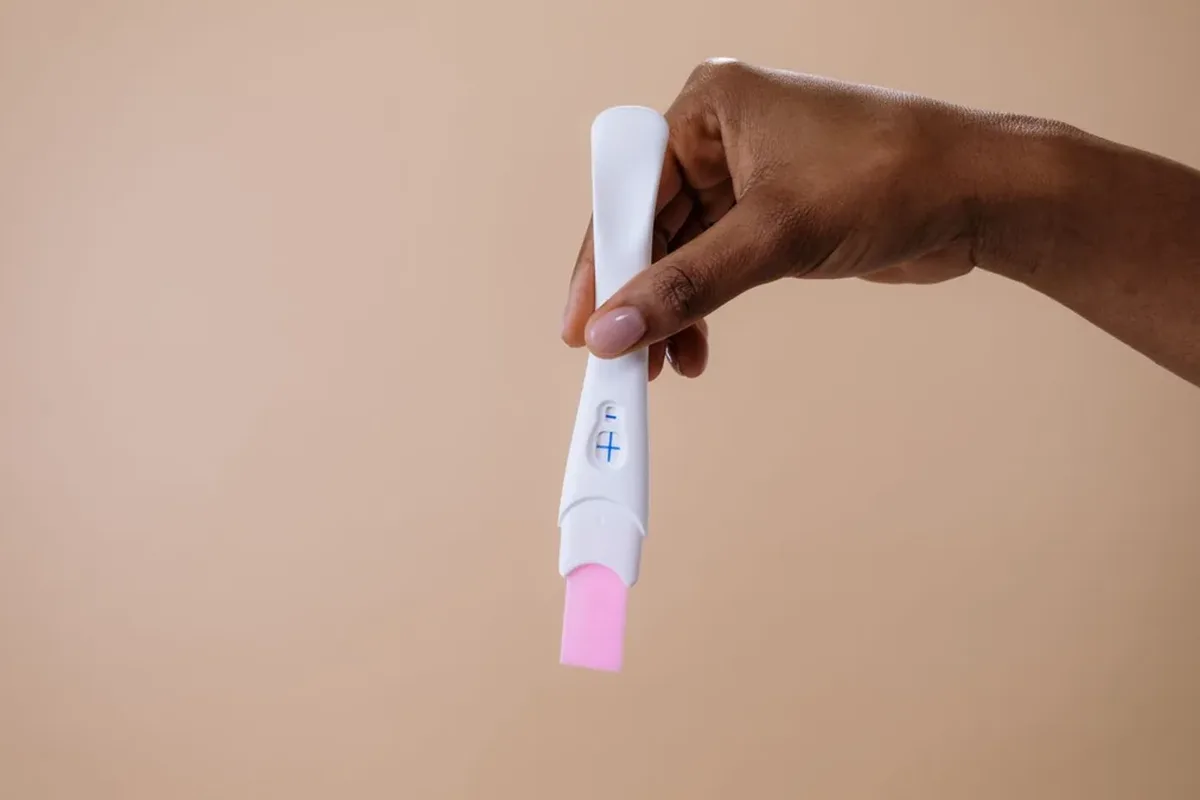 A hand holding a pregnancy test stick against a plain background