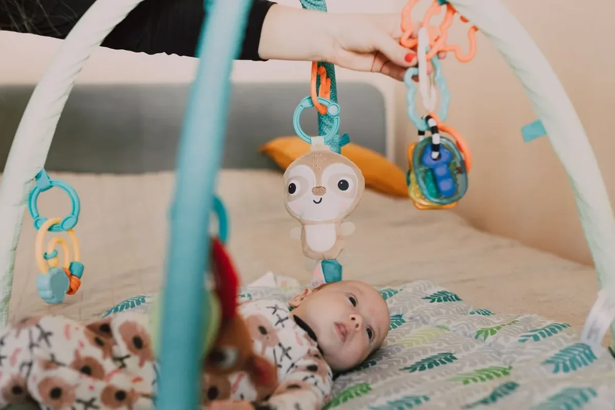 A baby lying on a play mat under a hanging toy arch
