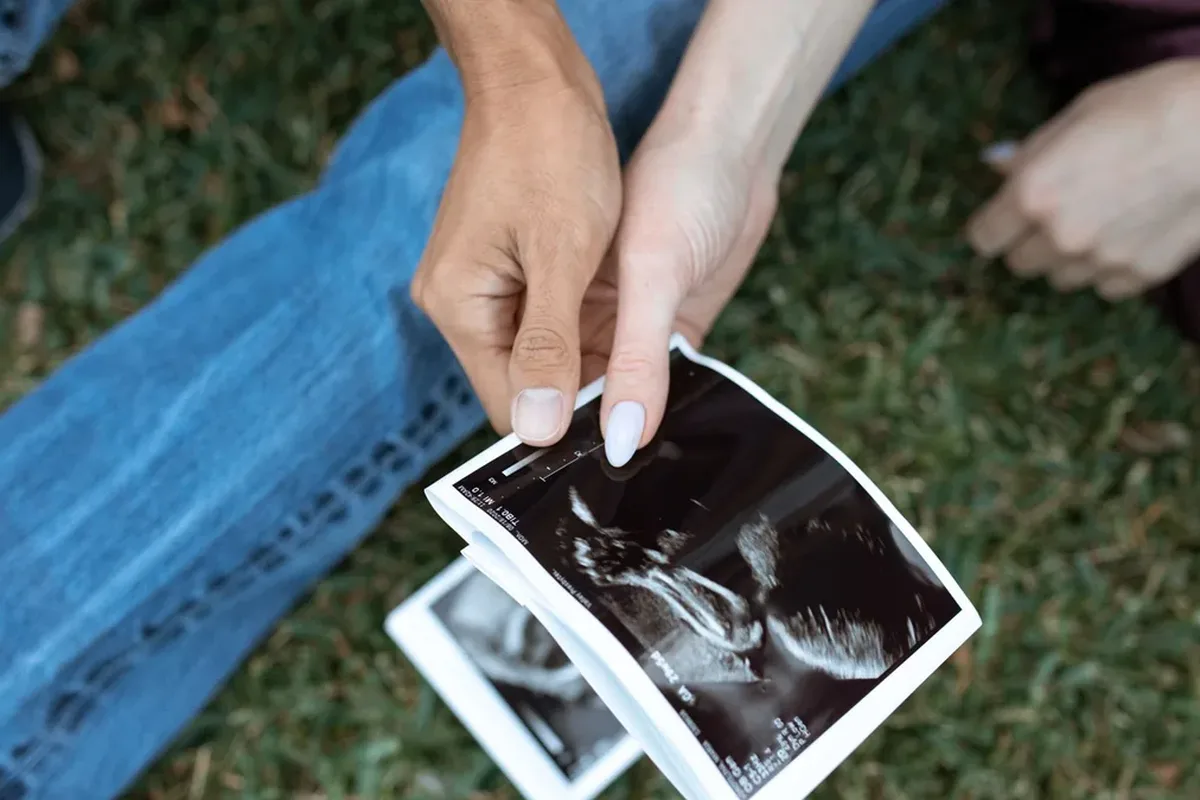 Two people's hands holding a black-and-white ultrasound scan photo